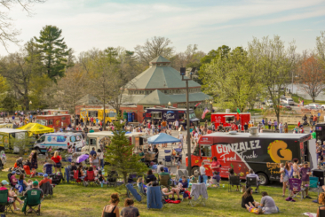 Food Trucks set up for Food Truck Fridays with guests walking around enjoying food and beverages at the event. Some guests are sitting in the grass or in chairs mingling with family and friends.