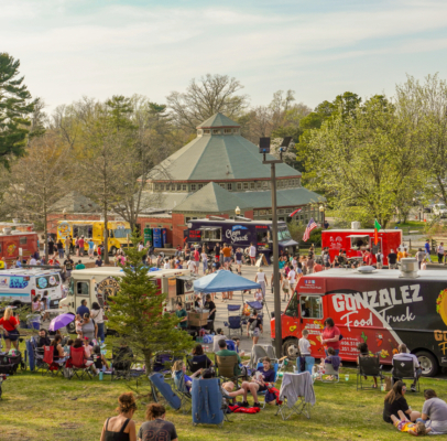 Food Trucks set up for Food Truck Fridays with guests walking around enjoying food and beverages at the event. Some guests are sitting in the grass or in chairs mingling with family and friends.