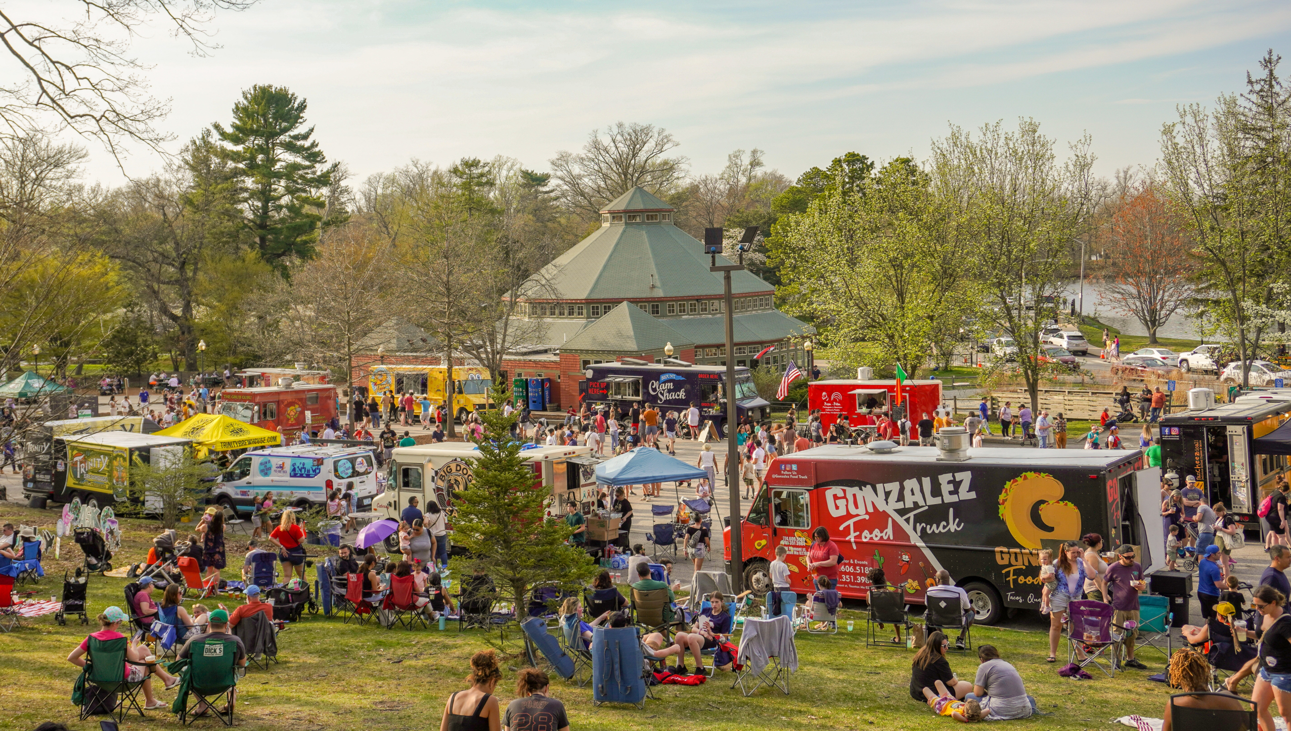 Food Trucks set up for Food Truck Fridays with guests walking around enjoying food and beverages at the event. Some guests are sitting in the grass or in chairs mingling with family and friends.