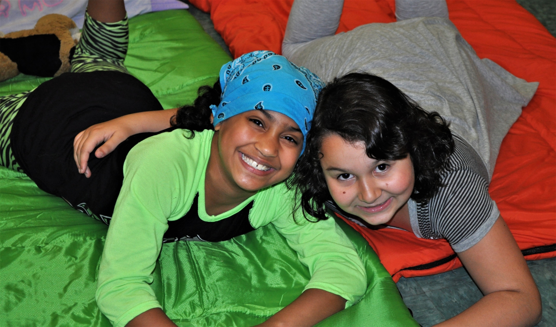 Two children smiling and posing for picture while laying on their sleeping bags at the Snore and Roar Overnight at the Zoo.