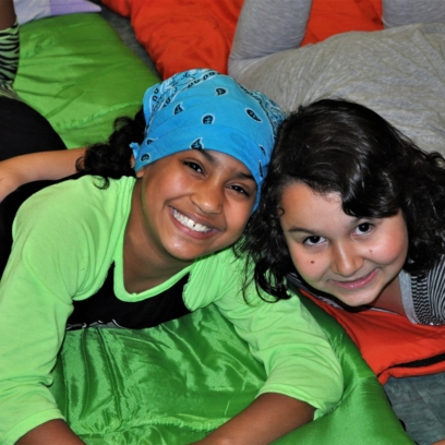 Two children smiling and posing for picture while laying on their sleeping bags at the Snore and Roar Overnight at the Zoo.