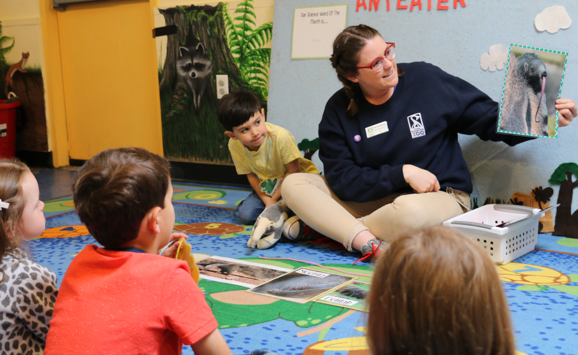 Zoo Education Staff during early childhood program showing a picture of an anteater to four children.