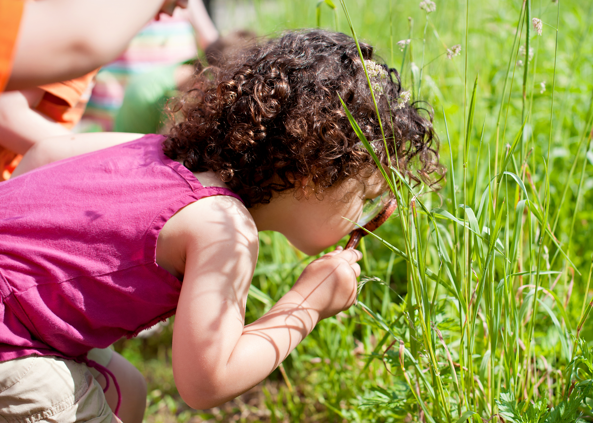 A child holding a magnifying glass looking for bugs in the grass.