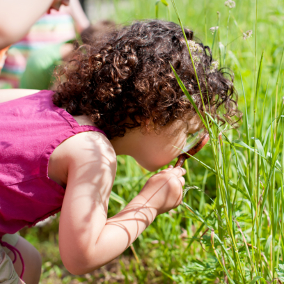 A child holding a magnifying glass looking for bugs in the grass.