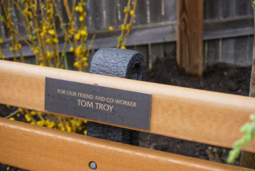 Close up of commemorate memorial bench with sign that says "for our friend and co-worker Tom Troy."
