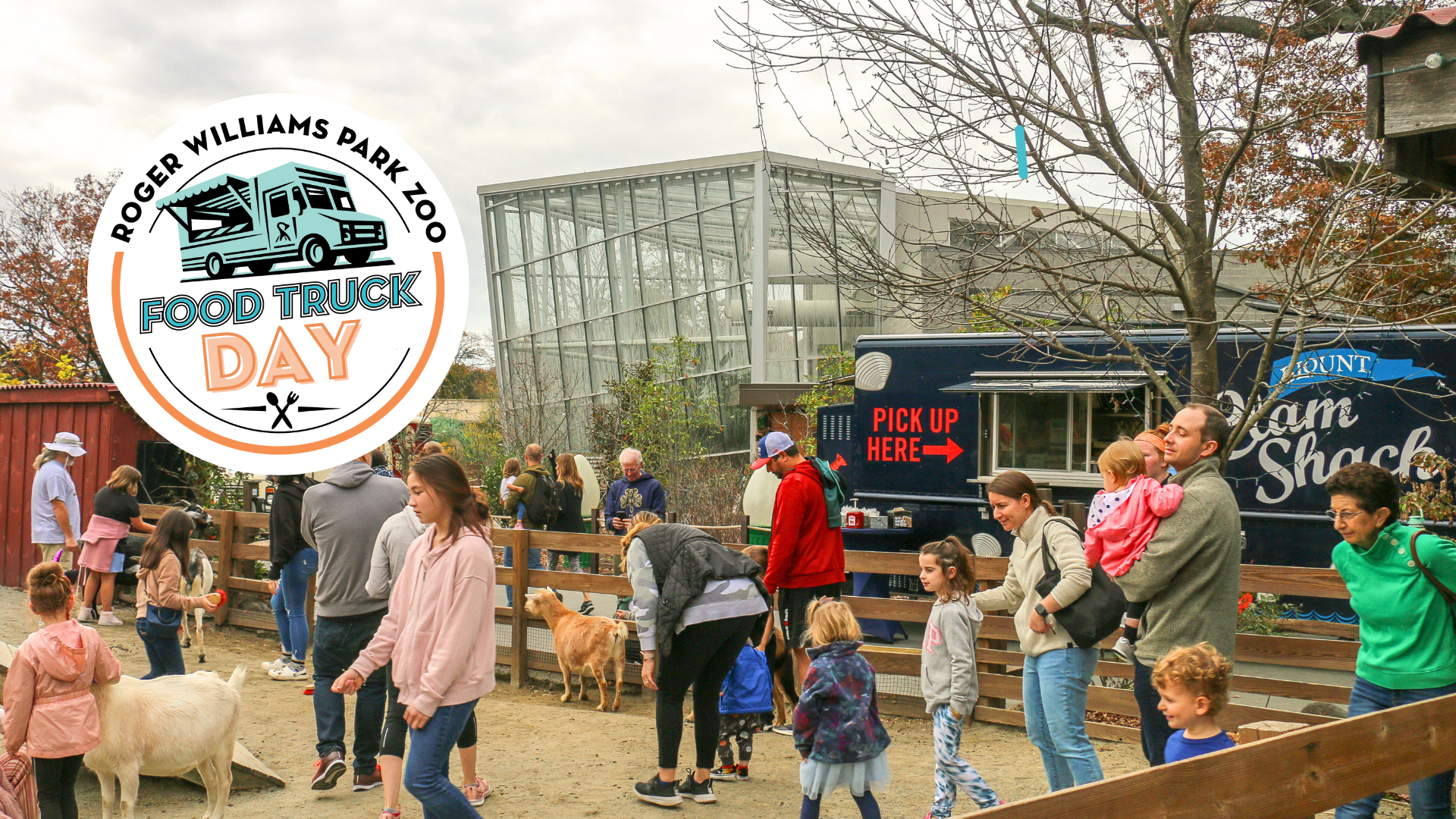 People petting goats at the Zoo, with food trucks in background.