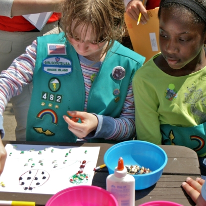 Two girl scouts sitting at a table doing crafts.