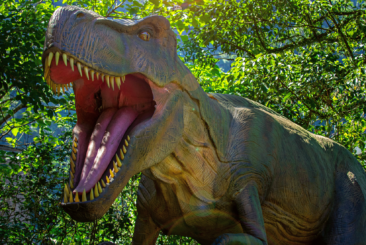 Graphic of T-Rex dinosaur with wide open mouth showing teeth with trees in the background.