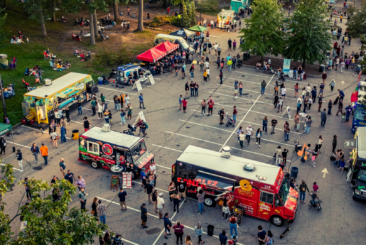 Food Trucks set up for Food Truck Fridays with guests walking around enjoying food and beverages at the event. Some guests are sitting in the grass or in chairs mingling with family and friends.