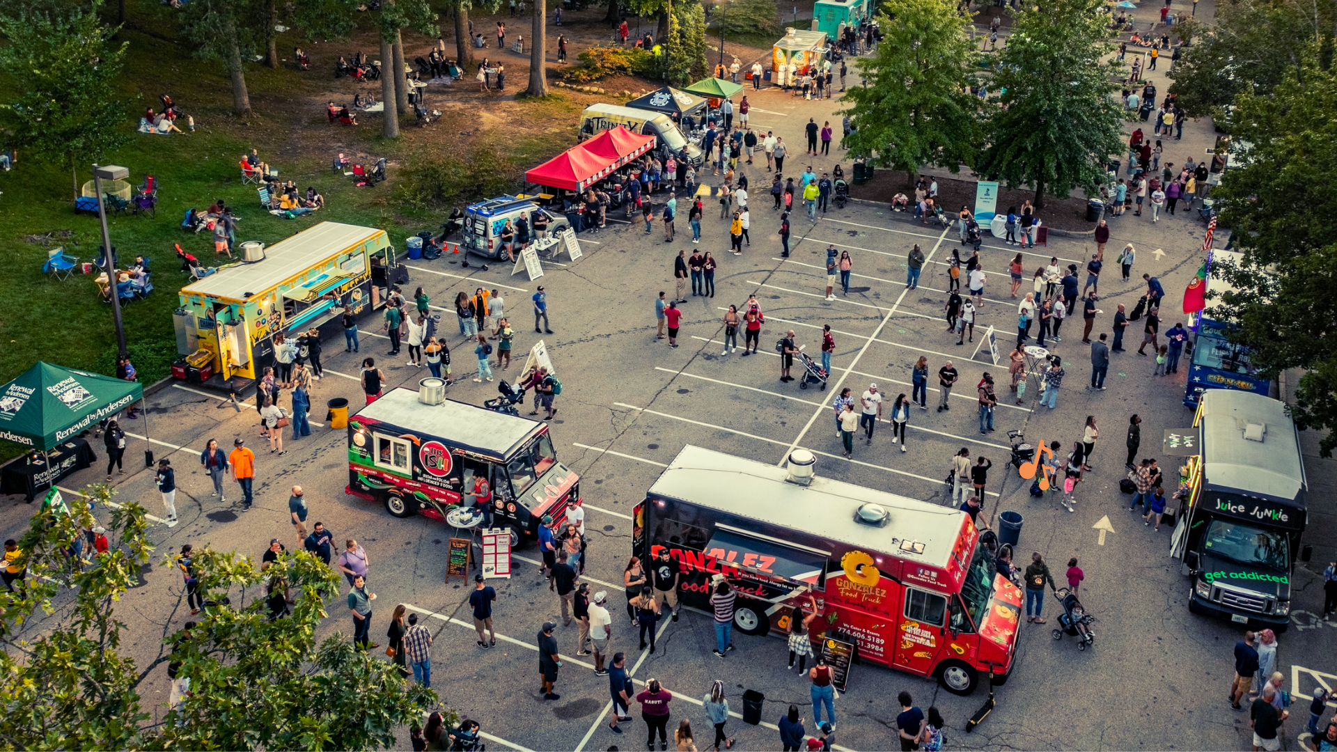 Food Trucks set up for Food Truck Fridays with guests walking around enjoying food and beverages at the event. Some guests are sitting in the grass or in chairs mingling with family and friends.