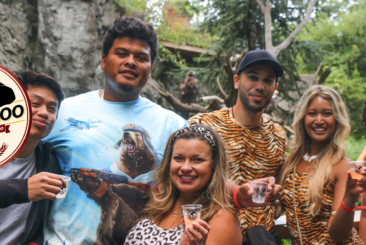 10 Years Brew at the Zoo logo in front of guests attending Brew at the Zoo event. Guests are dressed in animal print and holding tasting cups.