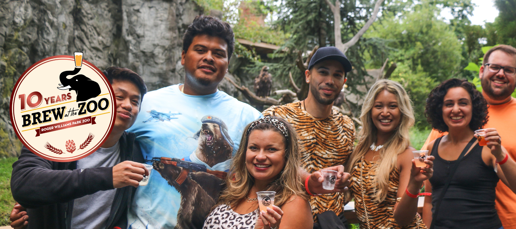 10 Years Brew at the Zoo logo in front of guests attending Brew at the Zoo event. Guests are dressed in animal print and holding tasting cups.