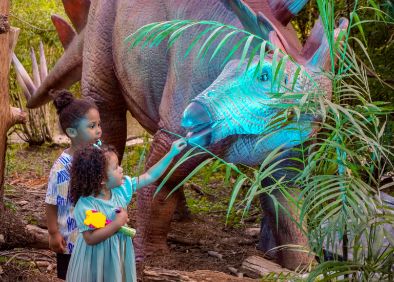 two young children looking at and interacting with a dinosaur at Dinos at Dusk