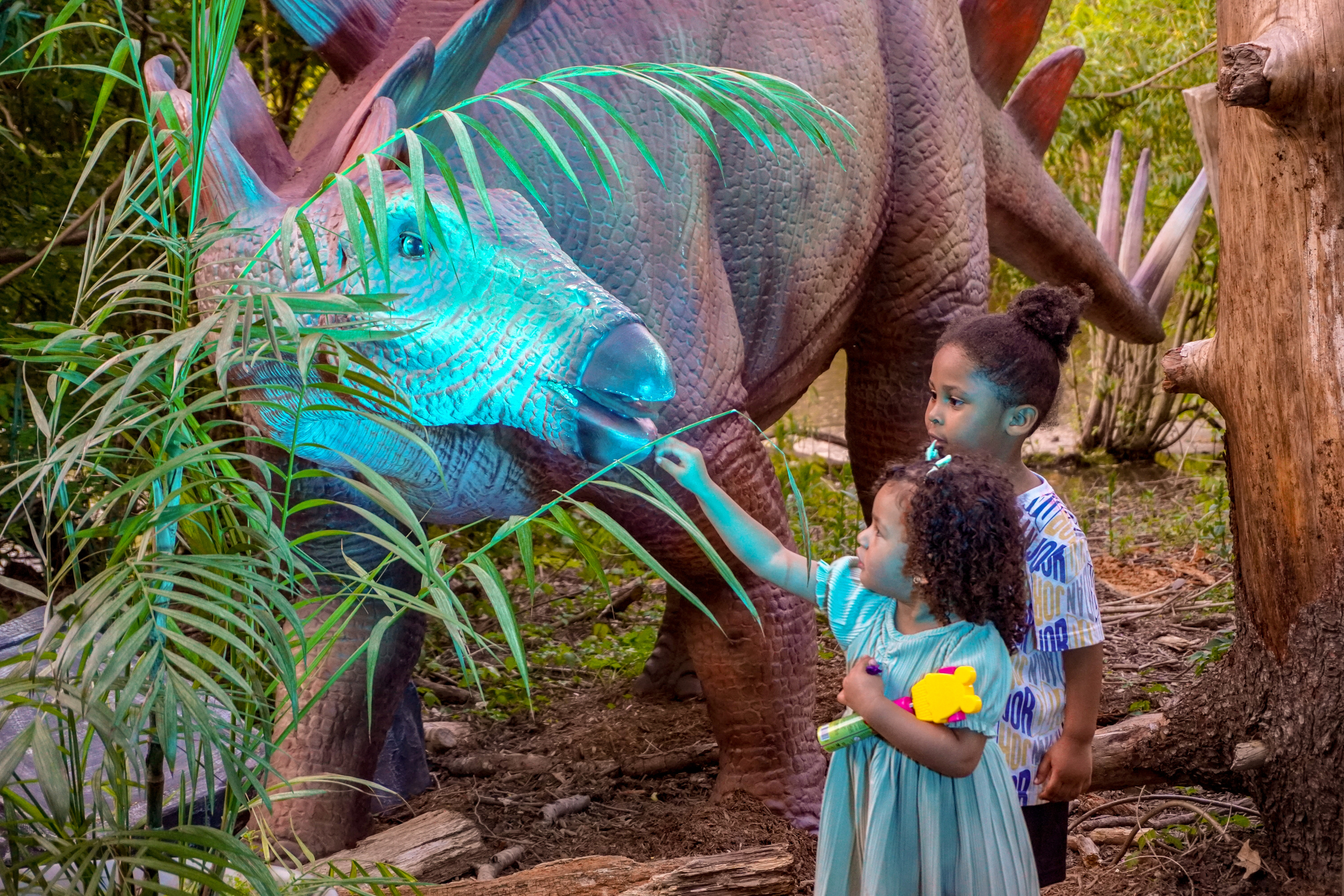two children with an animatronic dinosaur lit up at dusk
