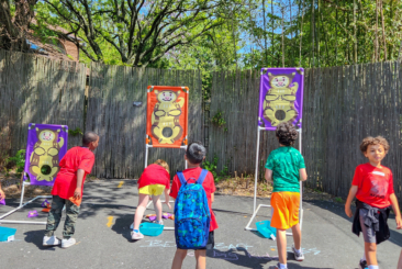 young children playing toss with tree kangaroo pouch game outside